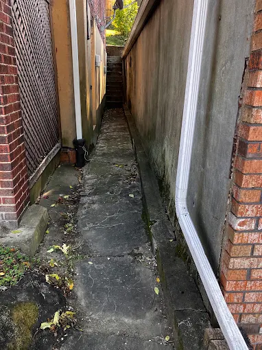 Cracked, mossy old walkway between two brick houses before replacement